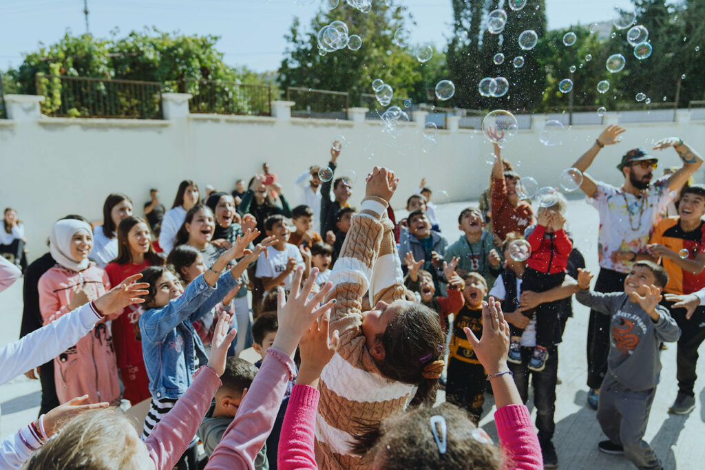 Children and adults celebrating in a vibrant Greek village, with bubbles, symbolizing community revival and hope against demographic decline.